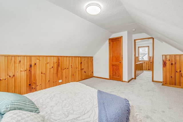 carpeted bedroom featuring vaulted ceiling, a textured ceiling, and wooden walls