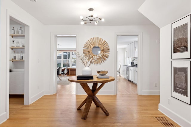 hallway with built in features, visible vents, baseboards, light wood-style flooring, and a chandelier