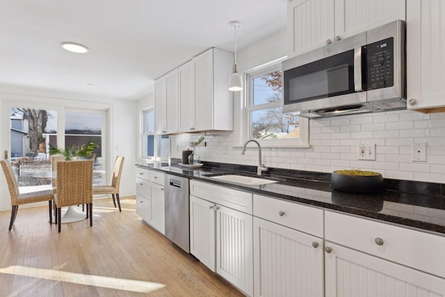 kitchen with a sink, white cabinets, hanging light fixtures, appliances with stainless steel finishes, and dark stone countertops