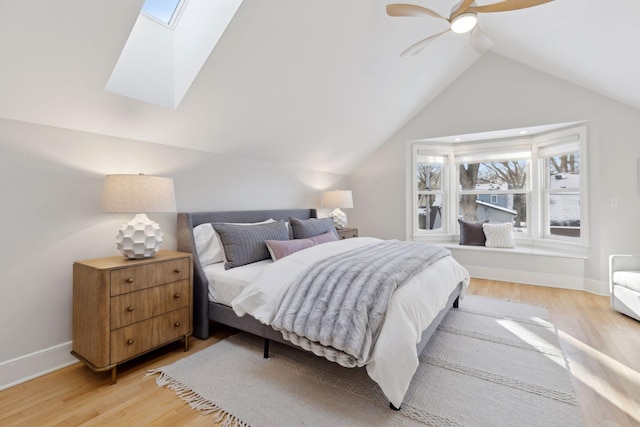 bedroom with baseboards, lofted ceiling with skylight, light wood-style flooring, and a ceiling fan