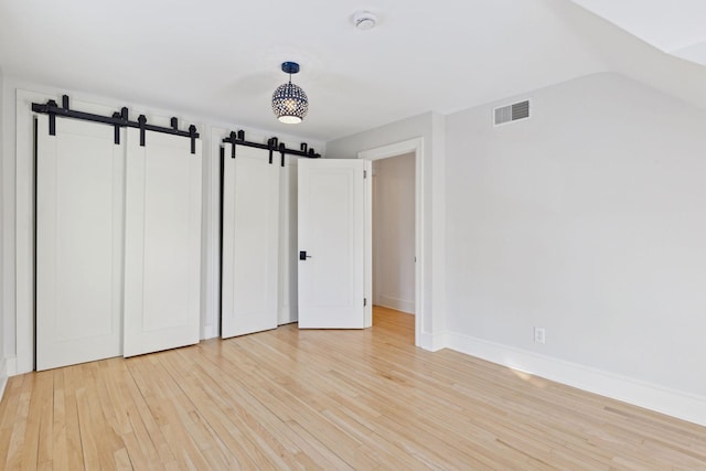 unfurnished bedroom featuring baseboards, a barn door, visible vents, and light wood-style floors