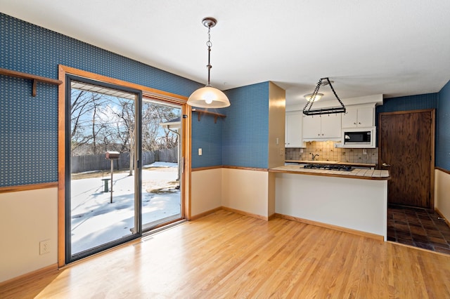 kitchen featuring wallpapered walls, a peninsula, built in microwave, white cabinetry, and light wood-type flooring