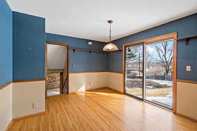 unfurnished room with a textured ceiling, wallpapered walls, baseboards, and wood finished floors