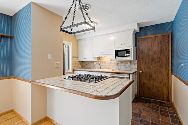 kitchen with built in microwave, gas cooktop, tile counters, and wallpapered walls