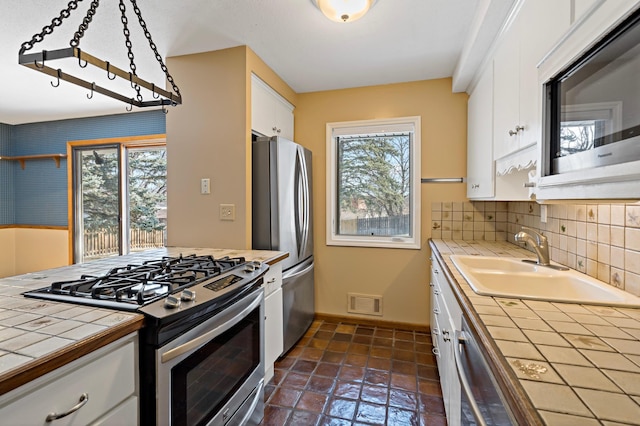 kitchen featuring visible vents, a healthy amount of sunlight, tile counters, appliances with stainless steel finishes, and white cabinetry