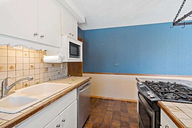 kitchen featuring tasteful backsplash, tile countertops, appliances with stainless steel finishes, white cabinets, and a sink