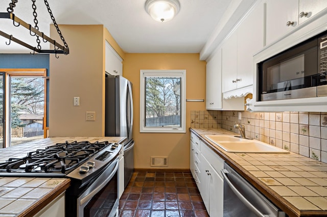 kitchen with visible vents, a sink, appliances with stainless steel finishes, white cabinets, and tile counters