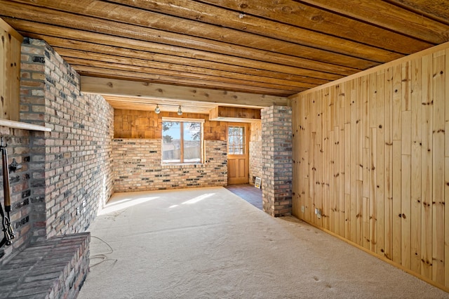 empty room with carpet floors, wooden walls, beam ceiling, and brick wall