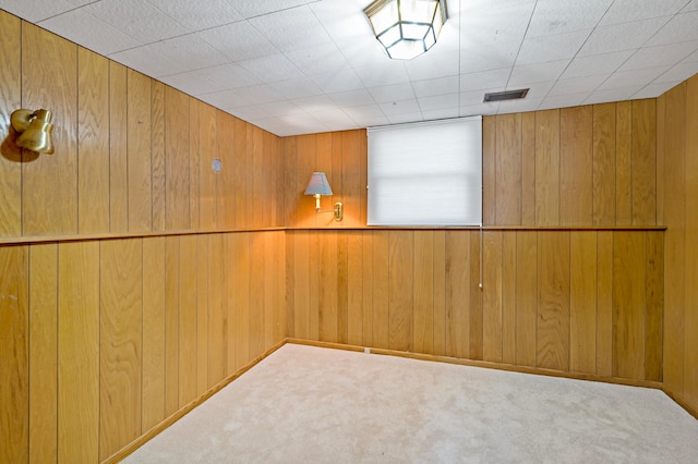 empty room featuring wooden walls, visible vents, and carpet floors