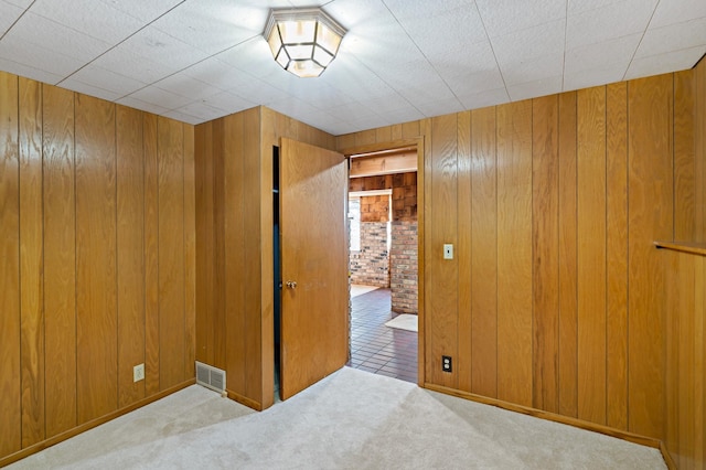 carpeted spare room featuring visible vents and wood walls