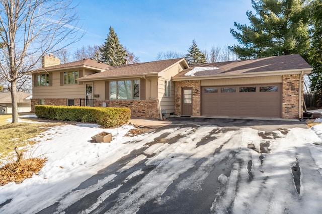 tri-level home featuring a garage, brick siding, driveway, and a chimney