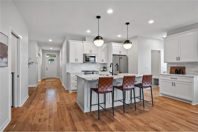 kitchen with white cabinetry, hanging light fixtures, a kitchen island with sink, stainless steel appliances, and light hardwood / wood-style floors