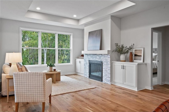 living room with a raised ceiling, a fireplace, and light hardwood / wood-style flooring