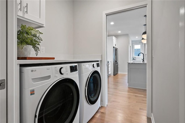 laundry room with washing machine and dryer, sink, and light hardwood / wood-style floors