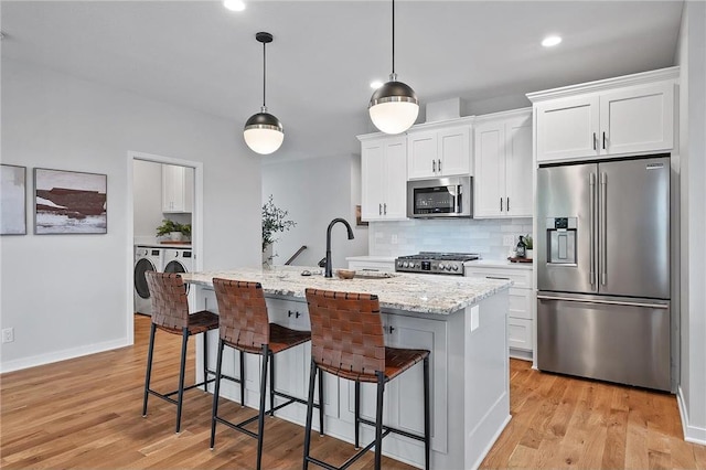 kitchen featuring washing machine and dryer, appliances with stainless steel finishes, a center island with sink, and white cabinets