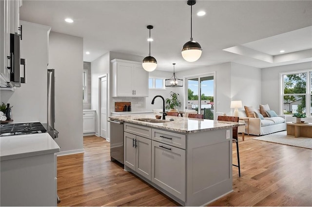 kitchen featuring sink, decorative light fixtures, an island with sink, stainless steel appliances, and white cabinets