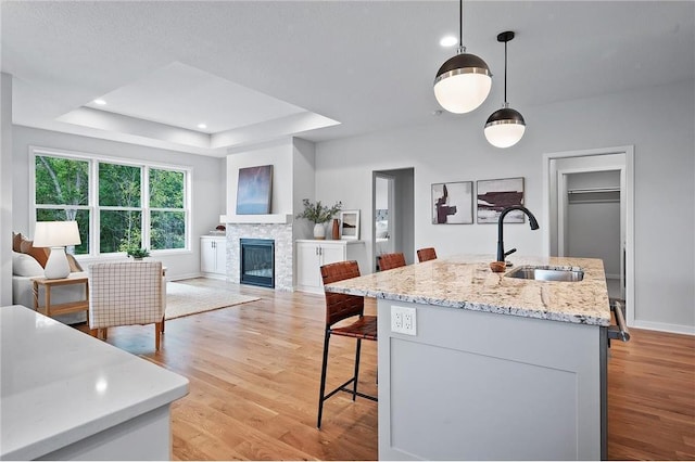 kitchen with decorative light fixtures, sink, a kitchen island with sink, a tray ceiling, and light stone countertops