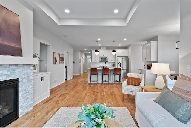 living room with a stone fireplace, light hardwood / wood-style floors, and a tray ceiling