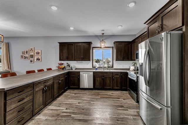 kitchen featuring a breakfast bar, hanging light fixtures, light wood-type flooring, stainless steel appliances, and decorative backsplash