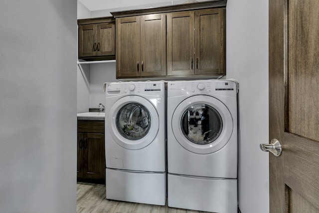 laundry room featuring cabinets, sink, washer and dryer, and light hardwood / wood-style flooring