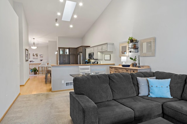 living room with a skylight, high vaulted ceiling, and light carpet