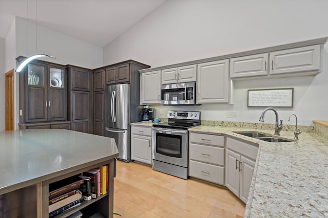 kitchen with appliances with stainless steel finishes, high vaulted ceiling, sink, light stone countertops, and light wood-type flooring