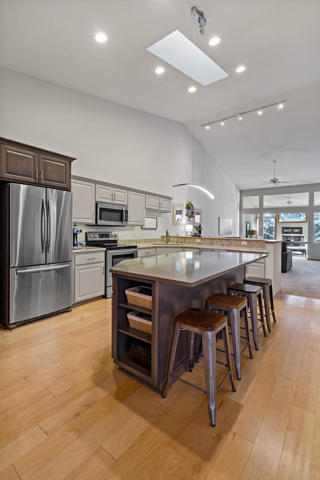 kitchen featuring a breakfast bar area, a skylight, light wood-type flooring, appliances with stainless steel finishes, and a kitchen island