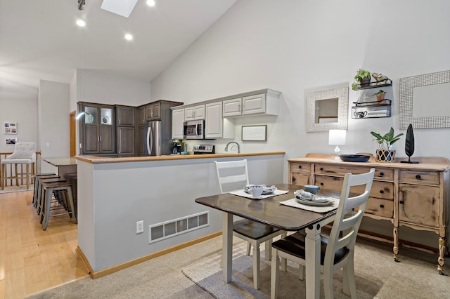 kitchen with high vaulted ceiling, a skylight, stainless steel appliances, and a breakfast bar