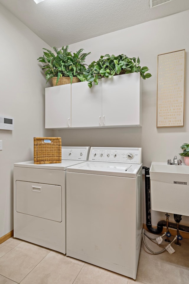 laundry room featuring washing machine and clothes dryer, sink, cabinets, a textured ceiling, and light tile patterned floors