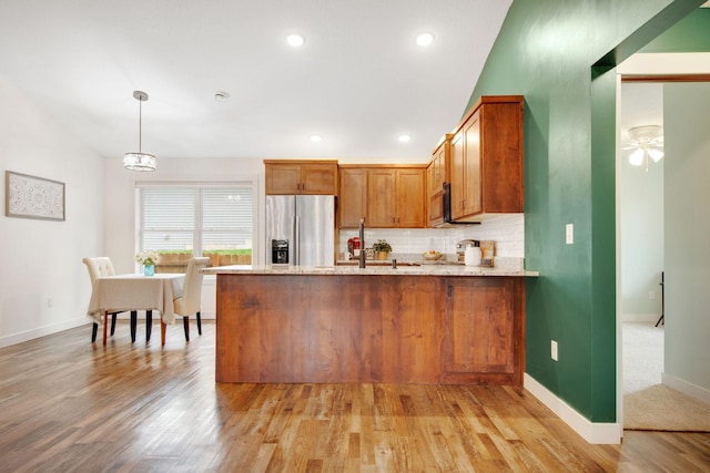 kitchen with pendant lighting, appliances with stainless steel finishes, light stone countertops, decorative backsplash, and kitchen peninsula