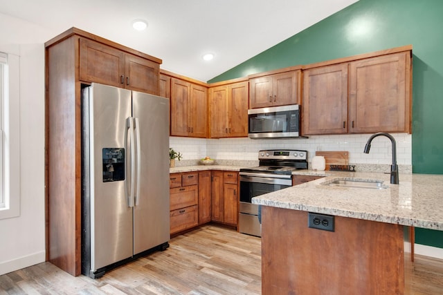 kitchen with lofted ceiling, sink, light stone counters, kitchen peninsula, and stainless steel appliances