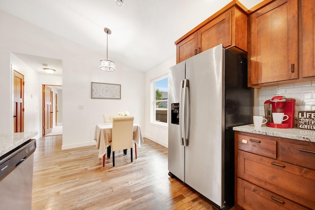 kitchen with appliances with stainless steel finishes, pendant lighting, lofted ceiling, backsplash, and light stone countertops