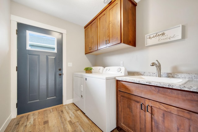 clothes washing area with cabinets, sink, washing machine and clothes dryer, and light wood-type flooring