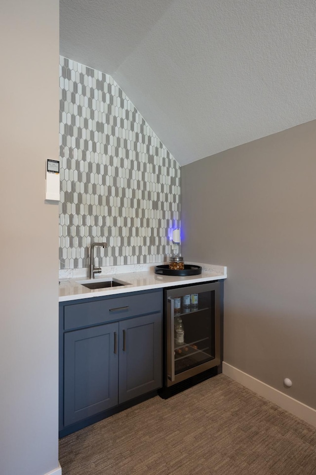 bar featuring sink, dark colored carpet, a textured ceiling, vaulted ceiling, and beverage cooler