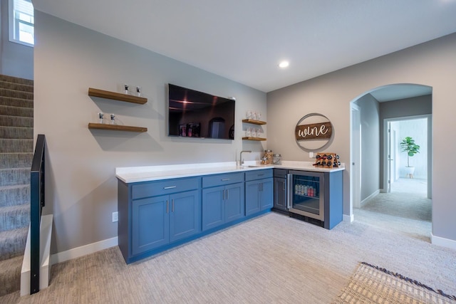 kitchen featuring sink, light colored carpet, beverage cooler, and blue cabinets