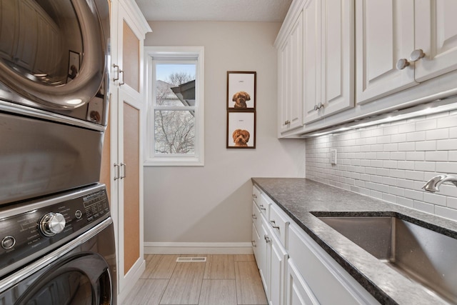 clothes washing area with visible vents, baseboards, stacked washing maching and dryer, a sink, and cabinet space