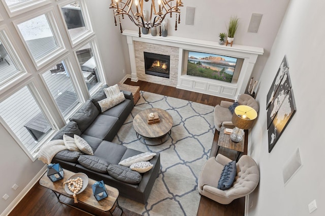 living area with a high ceiling, a notable chandelier, a fireplace, baseboards, and wood finished floors