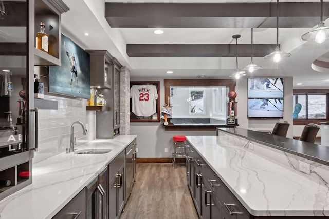 kitchen with a sink, baseboards, light wood-type flooring, backsplash, and pendant lighting
