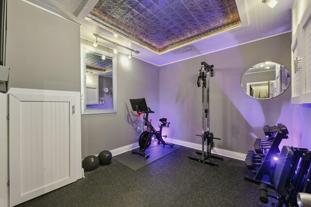 workout room with baseboards, a tray ceiling, and rail lighting