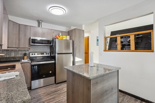 kitchen featuring light stone counters, backsplash, dark wood-type flooring, and stainless steel appliances