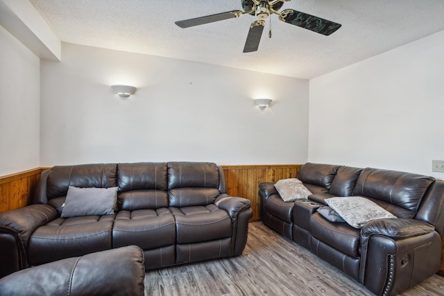 living room with ceiling fan, wooden walls, light hardwood / wood-style floors, and a textured ceiling