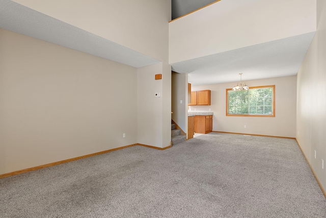 unfurnished living room with a towering ceiling, a chandelier, and light carpet