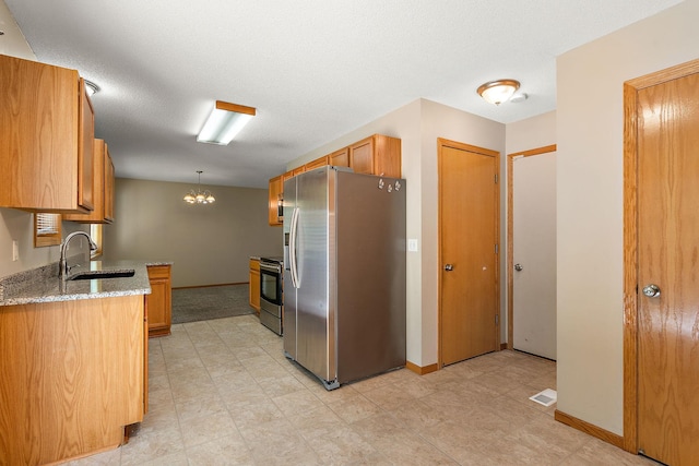 kitchen featuring sink, hanging light fixtures, stainless steel appliances, light stone counters, and a textured ceiling