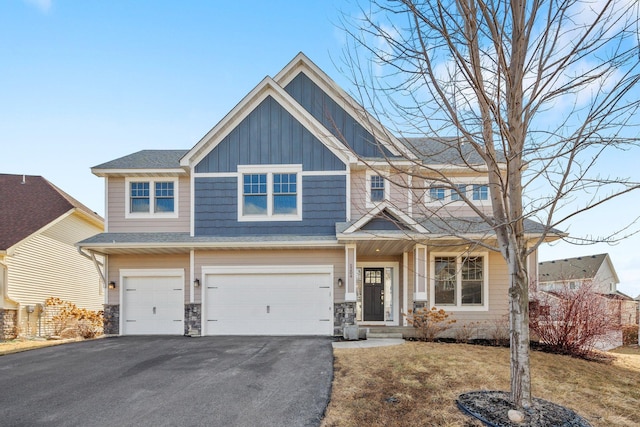 view of front facade with board and batten siding, stone siding, a garage, and aphalt driveway