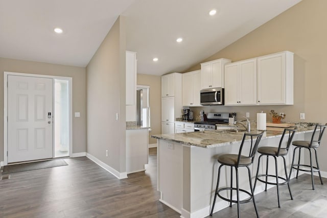 kitchen featuring appliances with stainless steel finishes, lofted ceiling, white cabinets, a kitchen breakfast bar, and kitchen peninsula