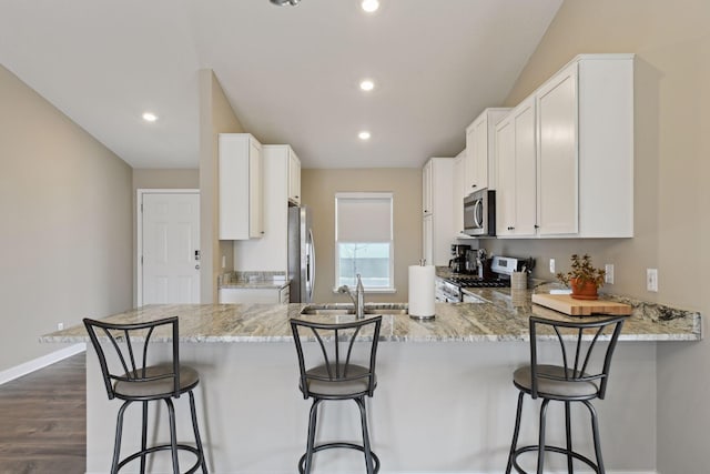 kitchen with sink, appliances with stainless steel finishes, white cabinets, a kitchen bar, and kitchen peninsula