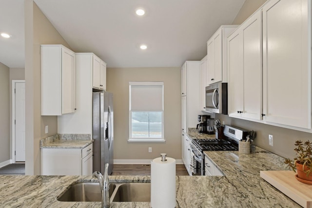 kitchen featuring sink, appliances with stainless steel finishes, hardwood / wood-style floors, light stone counters, and white cabinets