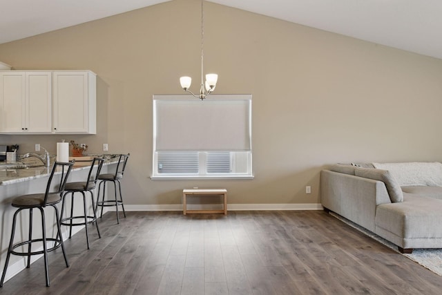 kitchen with vaulted ceiling, hardwood / wood-style floors, pendant lighting, white cabinetry, and a breakfast bar area