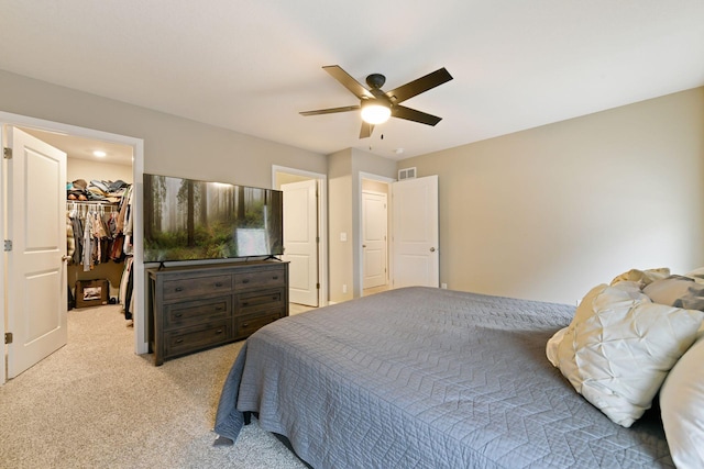 bedroom with a walk in closet, light colored carpet, a closet, and ceiling fan