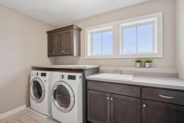 clothes washing area featuring cabinet space, washing machine and dryer, baseboards, and a sink